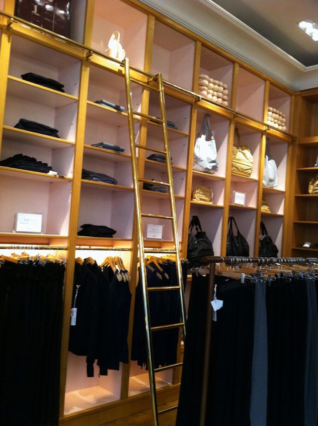 Un int&eacute;rieur de boutique &eacute;l&eacute;gant &agrave; l&rsquo;ambiance chaleureuse, dot&eacute; d&rsquo;une grande &eacute;chelle en bois fix&eacute;e &agrave; des &eacute;tag&egrave;res remplies de v&ecirc;tements