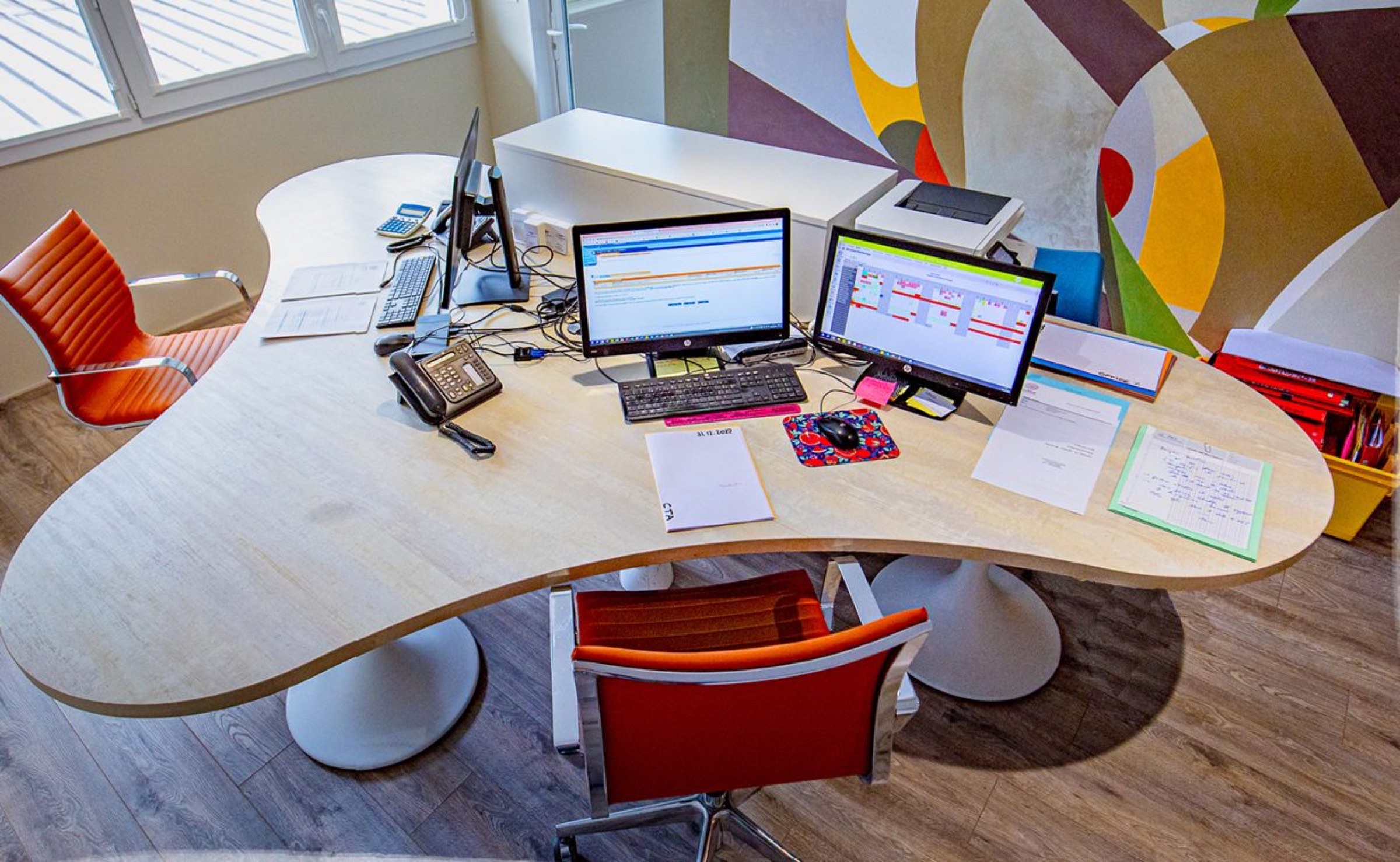 Espace de travail multit&acirc;che pour professionnel avec deux moniteurs, un bureau organis&eacute;, une d&eacute;coration de bureau color&eacute;e r&eacute;alis&eacute;e par un architecte d'int&eacute;rieur &agrave; Pau et une vari&eacute;t&eacute; de fournitures de bureau pr&ecirc;tes pour une journ&eacute;e productive.