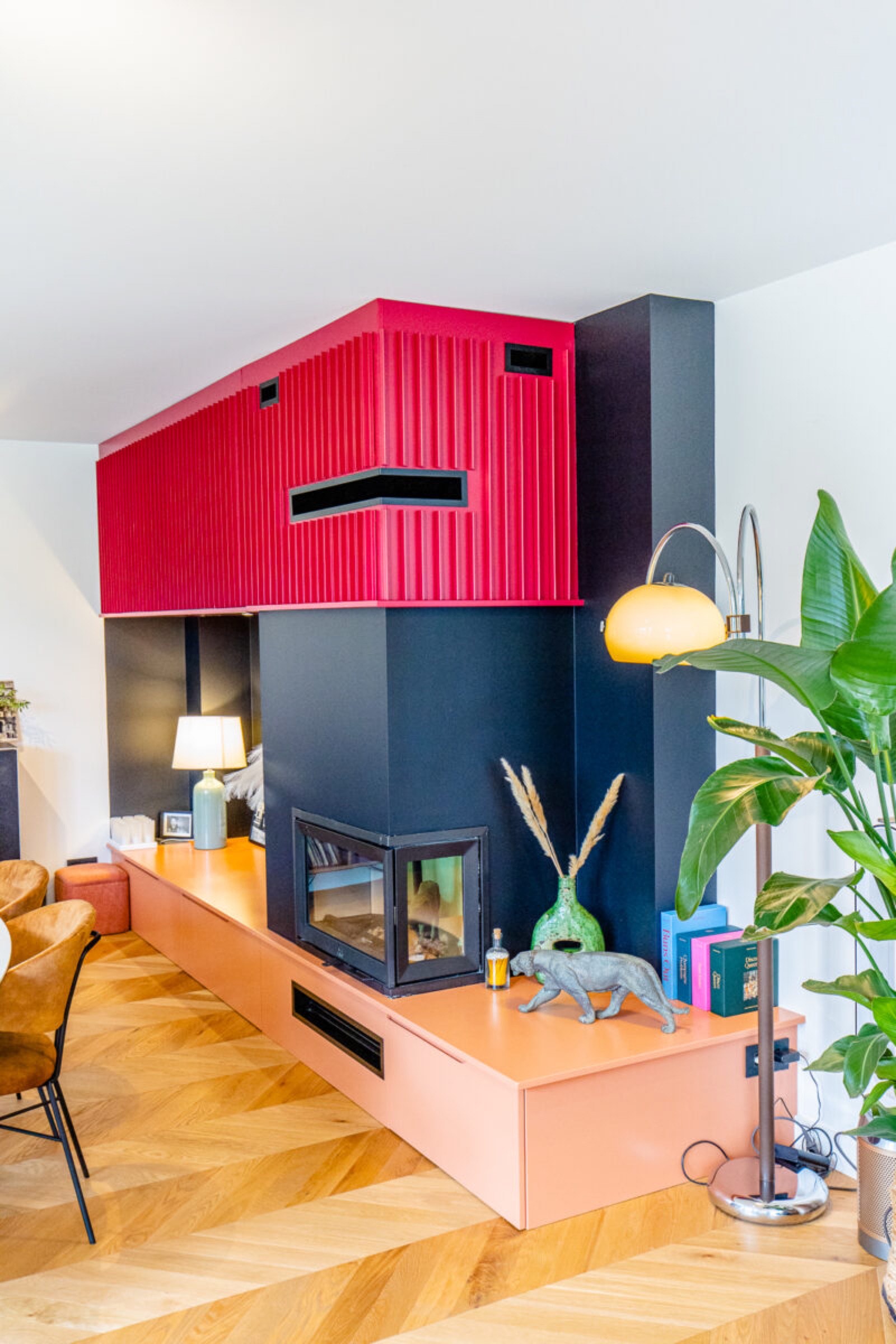 Salon moderne au décor vibrant de corail et de bleu marine, doté d'une cheminée élégante, d'un espace loft rose unique et d'une gamme de plantes d'intérieur créant une atmosphère à la fois chaleureuse et chic, se mariant parfaitement avec