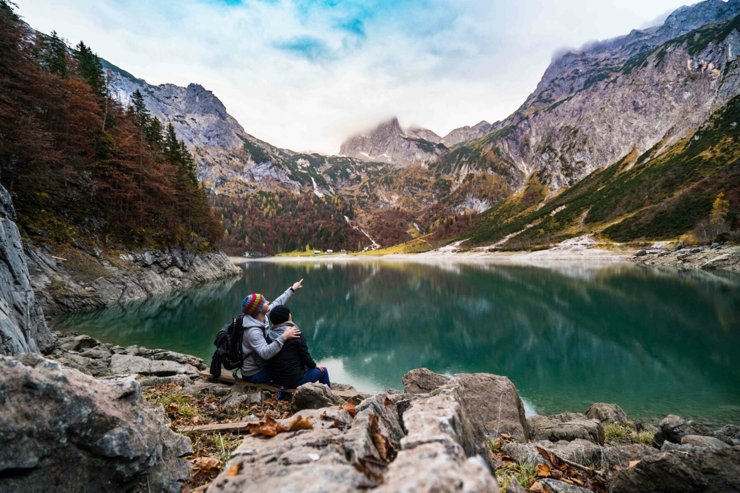Deux aventuriers faisant une pause au bord d'un lac de montagne serein, une personne montrant au loin quelque chose d'intéressant à son compagnon au milieu d'un magnifique paysage automnal. Il est intéressant de noter qu'ils discutaient de l'intention de consulter un