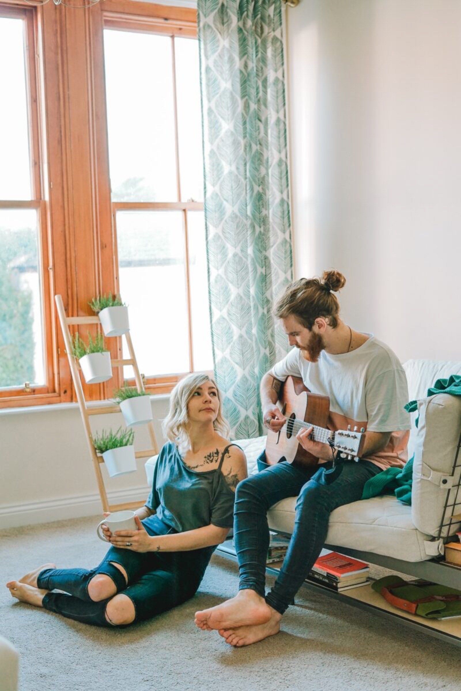 Un apr&egrave;s-midi cosy &agrave; la maison avec un homme qui joue de la guitare tandis qu'une femme assise &agrave; c&ocirc;t&eacute; de lui l'&eacute;coute attentivement dans un salon ensoleill&eacute; con&ccedil;u par un architecte d'int&eacute;rieur &agrave; Tarbes.
