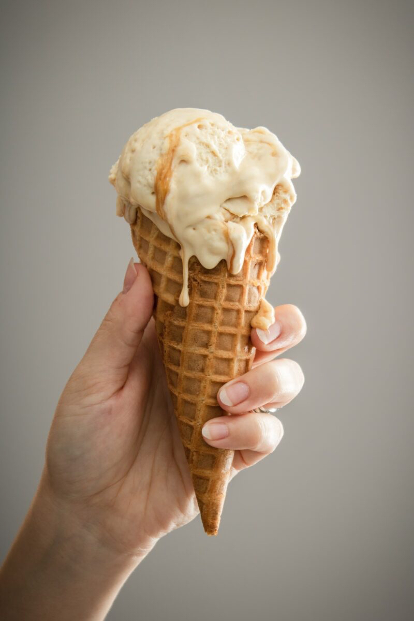 Une main tenant un cornet de glace à la vanille fondante provenant d'un glacier professionnel sur un fond neutre.