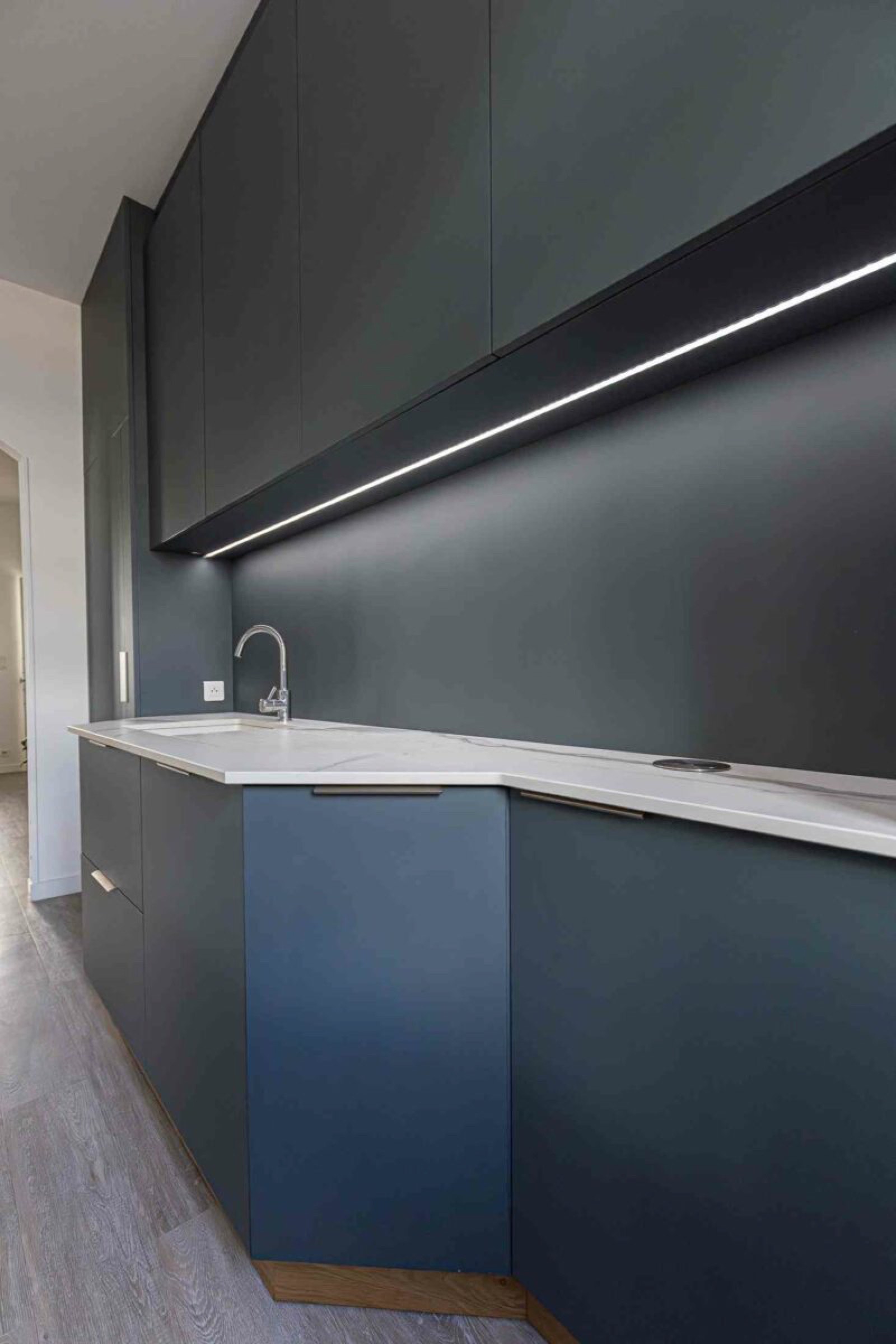 Une cuisine moderne avec des armoires &eacute;l&eacute;gantes gris fonc&eacute; et un design minimaliste. Elle comprend un &eacute;clairage sous les armoires, un comptoir blanc et un robinet en acier inoxydable. Adoptant les tendances de la d&eacute;coration pour l'am&eacute;nagement 2025, la cuisine pr&eacute;sente un look &eacute;pur&eacute; et contemporain avec une esth&eacute;tique minimaliste.