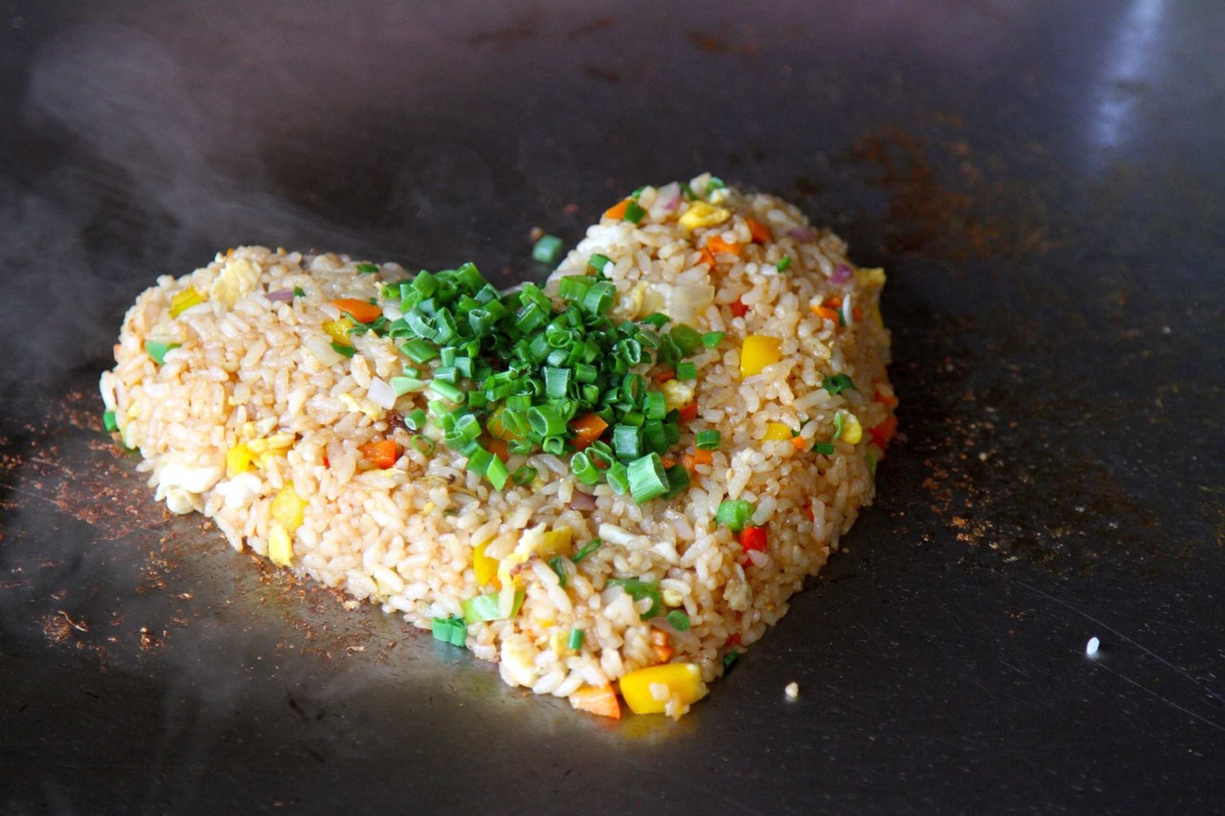 Riz frit fumant en forme de c&oelig;ur avec des l&eacute;gumes color&eacute;s garni d'oignons verts sur une surface de cuisson cocooning.