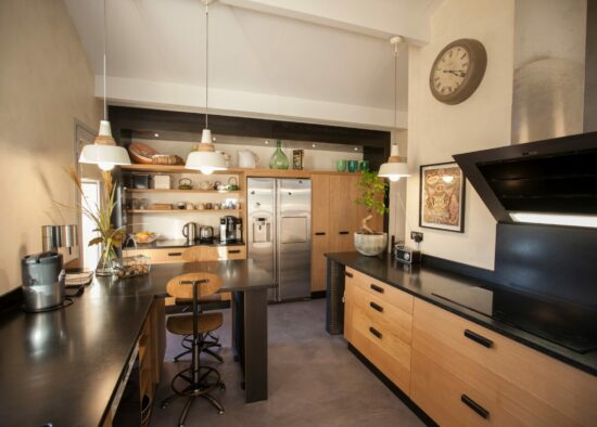 Un intérieur de cuisine moderne avec des comptoirs noirs élégants, des armoires en bois, des appareils électroménagers en acier inoxydable et un agencement professionnel sur un îlot avec des tabourets de bar.