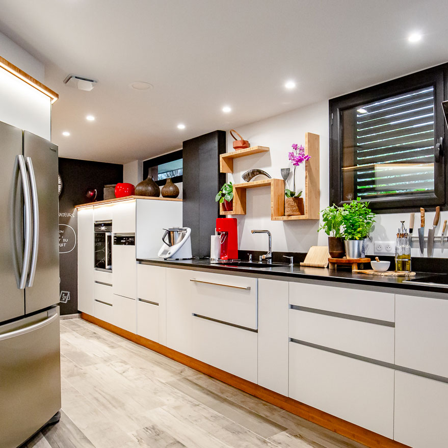 Une cuisine moderne avec des armoires blanches élégantes, des appareils électroménagers en acier inoxydable et un parquet élégant, avec des touches de couleur provenant de plantes et d'objets décoratifs.