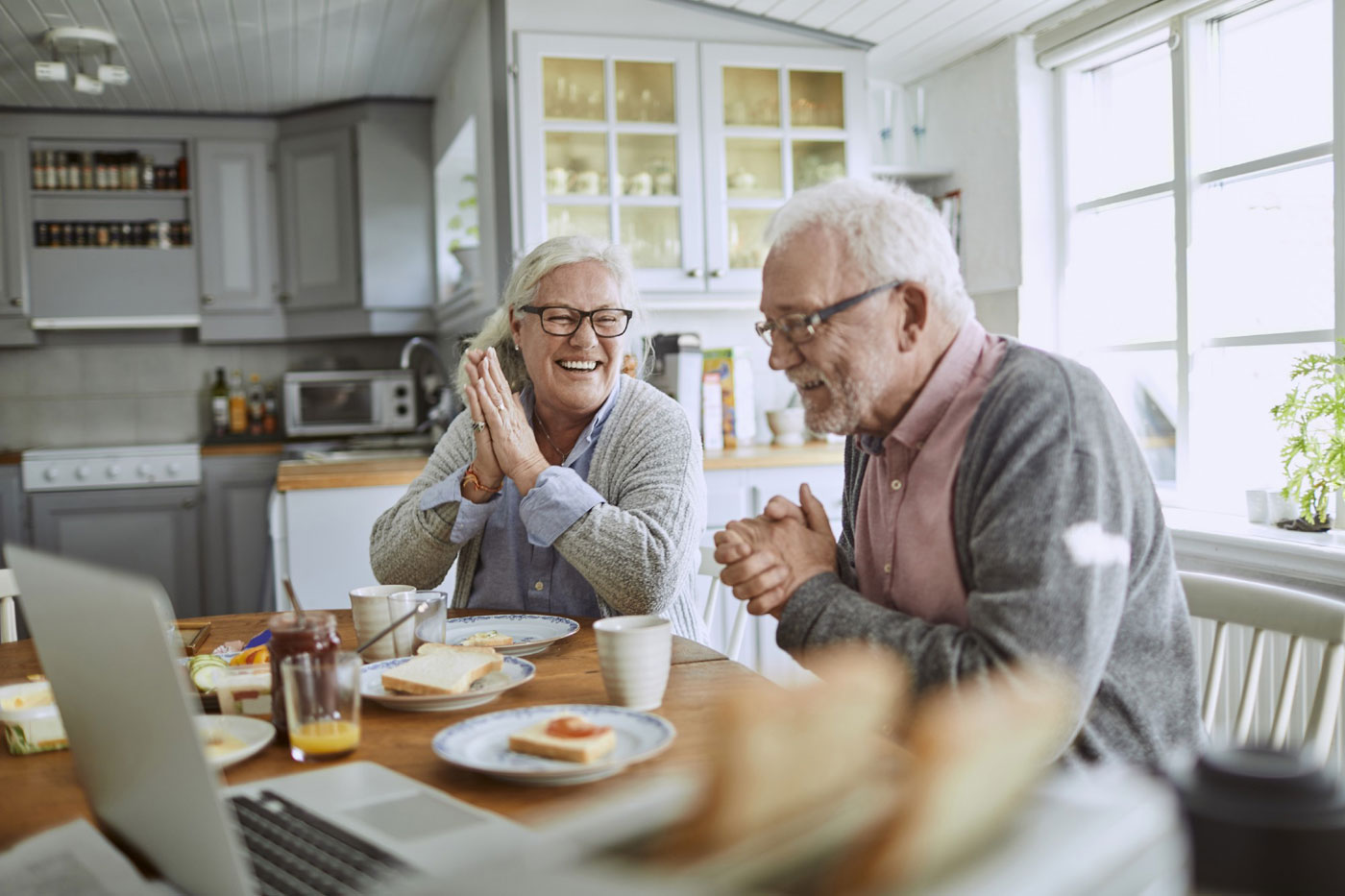 Un joyeux couple de seniors partageant un moment ludique autour du petit-déjeuner dans une cuisine lumineuse et cosy, conçue avec un agencement pensé pour la mobilité.