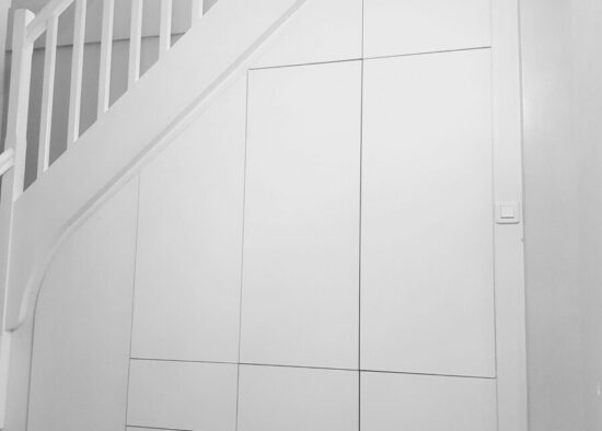 Rangement sous l'escalier avec des portes blanches épurées parfaitement intégrées dans un intérieur de maison moderne par un architecte d'intérieur à Tarbes.