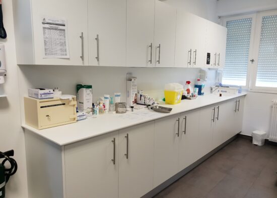 Un espace de travail de laboratoire bien organisé avec des armoires blanches, diverses bouteilles, du matériel de laboratoire et des documents sur mesure répartis sur le comptoir.