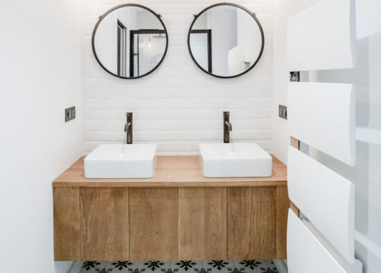 Une salle de bain moderne comprenant deux vasques avec vasque flottante en bois, deux miroirs ronds, du carrelage métro blanc au mur et un sol à motifs conçu par un architecte d'intérieur de Tarbes.