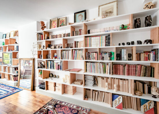 Une bibliothèque d'espace de vie cosy et personnalisée, conçue par un architecte d'intérieur à Tarbes, remplie d'une collection éclectique de livres, d'objets et d'œuvres d'art encadrées, invitant à un voyage de l'esprit.