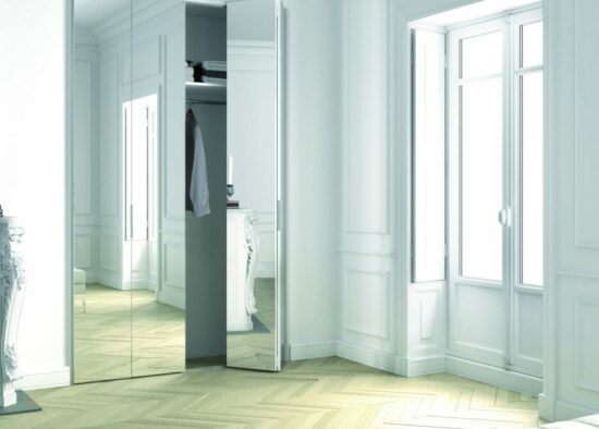 Une salle lumineuse et moderne avec un parquet en chevrons, d'élégantes lambris blancs et un grand miroir reflétant une porte ouverte menant à une cuisine soignée sur mesure à Tarbes.