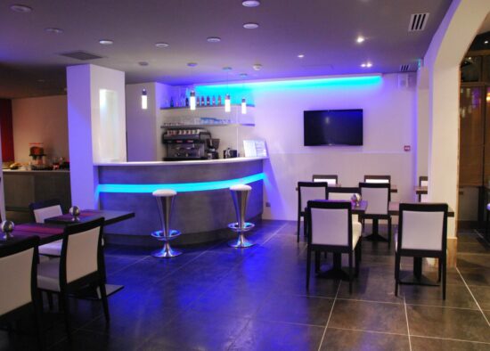Intérieur de café moderne avec éclairage d'accent bleu, comptoir de bar élégant, mobilier contemporain et cuisine sur mesure à Pau.