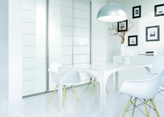 Une salle à manger épurée et moderne baignée de lumière naturelle, dotée d'un ensemble table et chaises blanches minimalistes, à la décoration artistique et d'un plafonnier unique conçu par un cuisiniste à Tarbes.