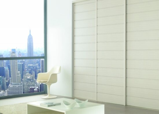 Espace de vie moderne et minimaliste avec une élégante chaise blanche et des meubles sur mesure, offrant une vue spectaculaire sur la ville à travers des baies vitrées.
