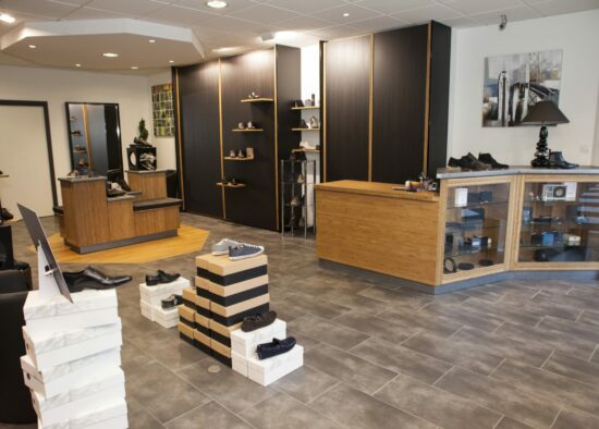 Un intérieur de magasin de chaussures bien organisé avec une gamme de chaussures élégantes sur des étagères et dans des boîtes au sol, avec un coin salon central pour les clients essayant les chaussures. L'agencement sur mesure