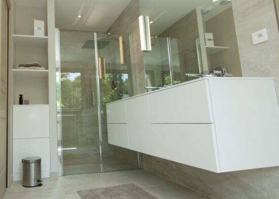 Une salle de bain moderne avec des armoires blanches élégantes, une cabine de douche en verre et des tons neutres créant une ambiance sereine et épurée, conçue par un architecte d'intérieur.