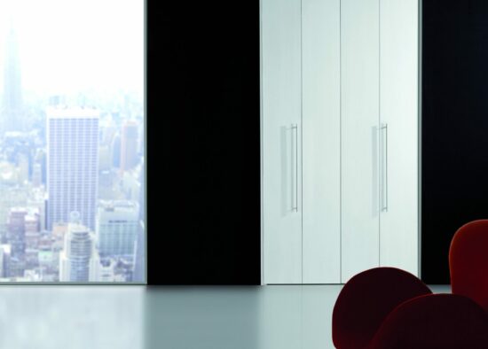 Bureau moderne au design minimaliste donnant sur un paysage urbain tentaculaire à travers une baie vitrée, doté d'armoires blanches élégantes et de meubles sur mesure, dont une chaise rouge vif comme accent audacieux.