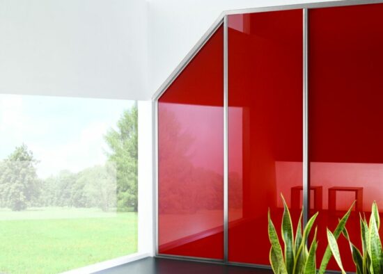 Intérieur moderne avec un mur de verre rouge vif donnant sur un jardin serein, où le style minimaliste rencontre la nature, conçu par un cuisiniste qualifié à Tarbes.