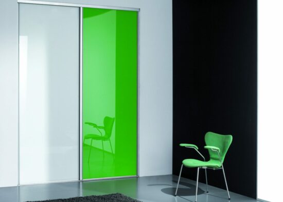 Une pièce minimaliste avec un contraste saisissant entre un panneau de verre vert vif et un environnement monochrome, avec une seule chaise verte élégante face à son reflet, conçue avec des meubles sur mesure pour mettre en valeur l'espace.