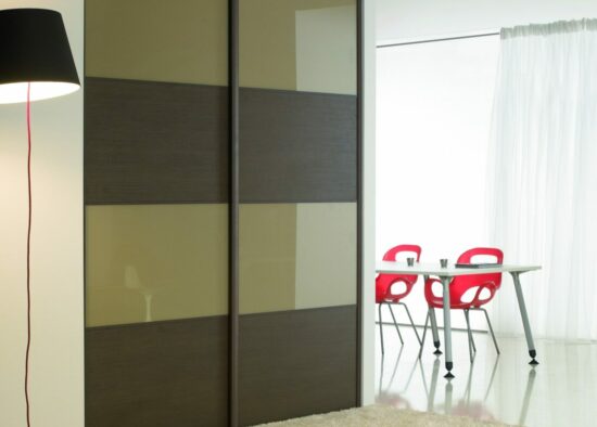 Une pièce moderne et minimaliste avec un grand lampadaire, une porte de placard coulissante avec des panneaux en verre dépoli et un petit coin repas doté de meubles sur mesure, dont une table blanche et des chaises rouges