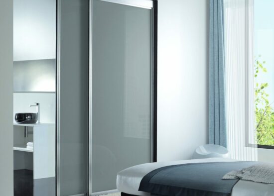 Une chambre moderne avec une élégante armoire à portes coulissantes reflétant une salle de bain lumineuse et minimaliste conçue par un architecte d'intérieur à Tarbes.