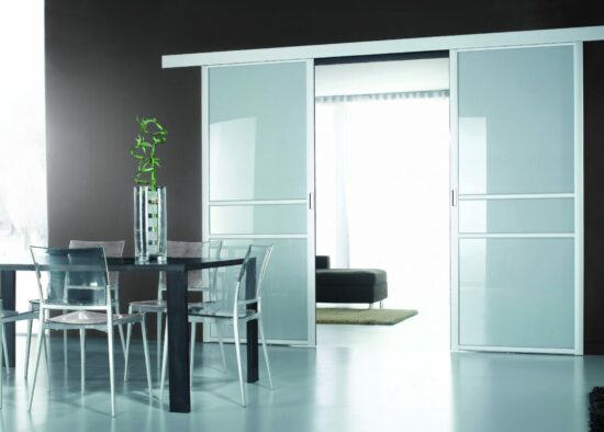 Une salle à manger moderne dotée d'une table et de chaises en verre élégantes, de grandes portes coulissantes blanches menant à une autre partie de la maison, complétée par un décor minimaliste et une palette de couleurs monochromes conçues par