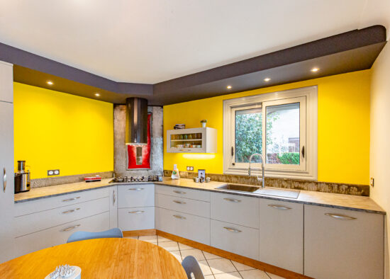 Cuisine moderne avec des murs jaune vif, des armoires grises élégantes et des appareils électroménagers en acier inoxydable, offrant un espace joyeux et contemporain pour la conception de la cuisine et les repas.