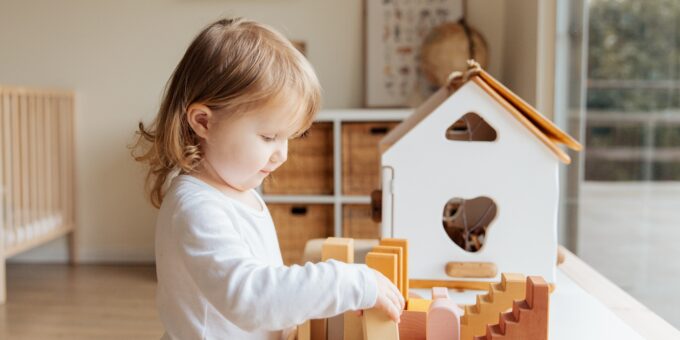 Un jeune enfant s'engageant dans un jeu avec une maison de jouets en bois et des blocs, faisant preuve de curiosité et de concentration, illustrant un sens précoce de l'agencement intérieur.