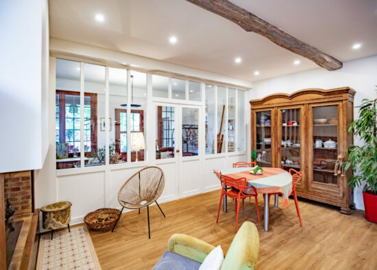 Une salle à manger lumineuse et confortable dans une maison de style rustique moderne avec une séparation de pièce en verre à cadre blanc, une poutre en bois apparente et des accents chaleureux, notamment une armoire en bois, un petit
