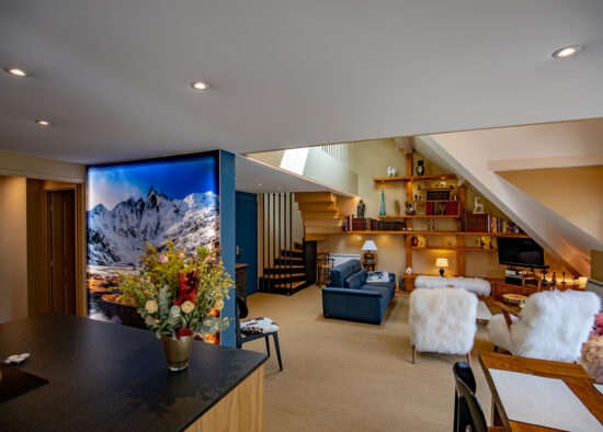Un espace de vie confortable et moderne comprenant une cuisine élégante avec vue sur un salon chaleureux et accueillant orné d'un grand paysage de montagne, des sièges confortables et un escalier élégant dans le cadre de son total.
