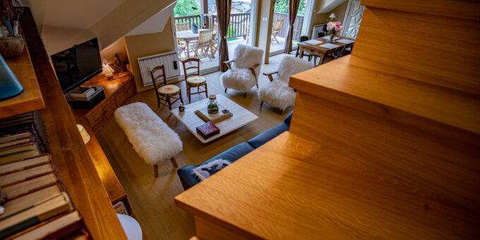 Un salon cosy et bien éclairé vu depuis l'escalier en bois, doté d'un mobilier confortable et d'une ambiance chaleureuse et accueillante, relooké par un architecte d'intérieur qualifié.