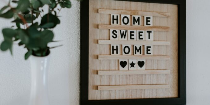 Un panneau en carton confortable et accueillant affichant l'expression « home sweet home » avec des symboles de cœur, placé sur un mur blanc à côté d'un vase avec de la verdure, parfaitement conçu par un architecte d'intérieur.