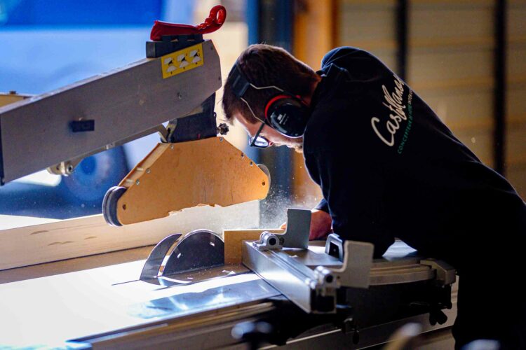 Un artisan utilise intensément une scie circulaire dans un poste de travail du bois, coupant un morceau de bois avec précision et concentration dans l'équipe d'agenceurs Castellanos.